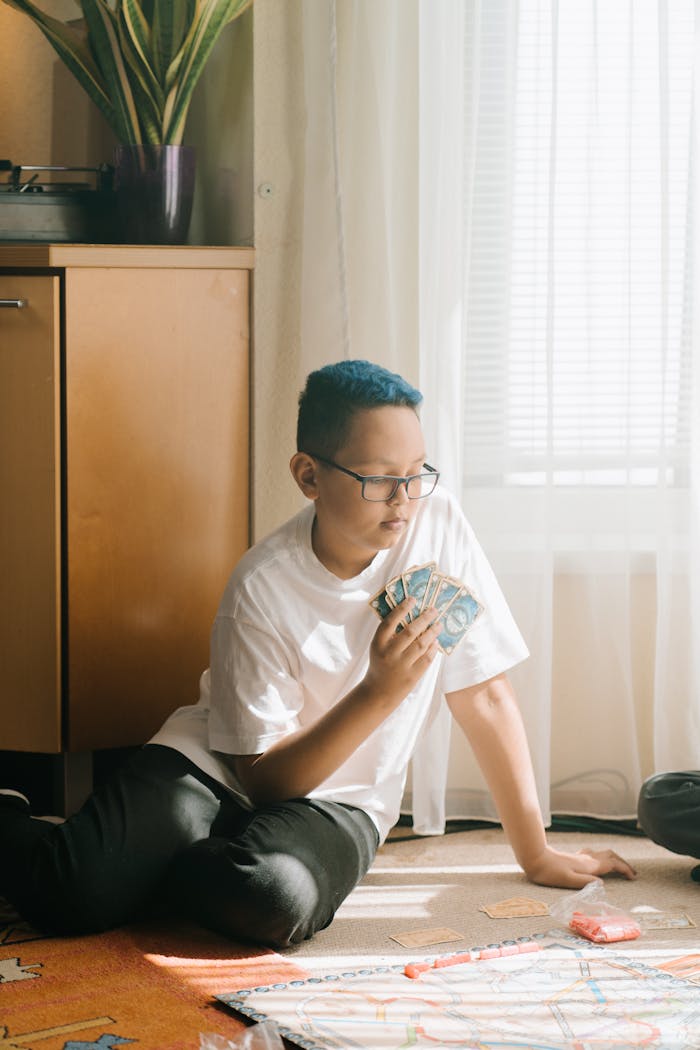 A boy with colored hair sits indoors, strategically playing a board game.