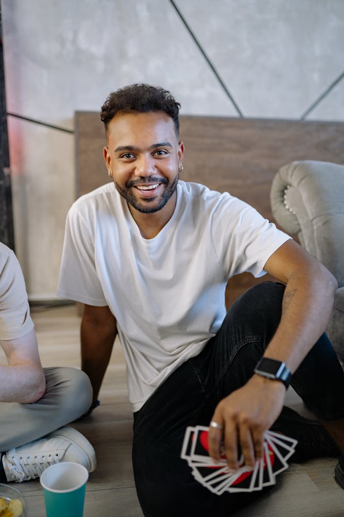 Smiling man holding cards while sitting on the floor indoors.